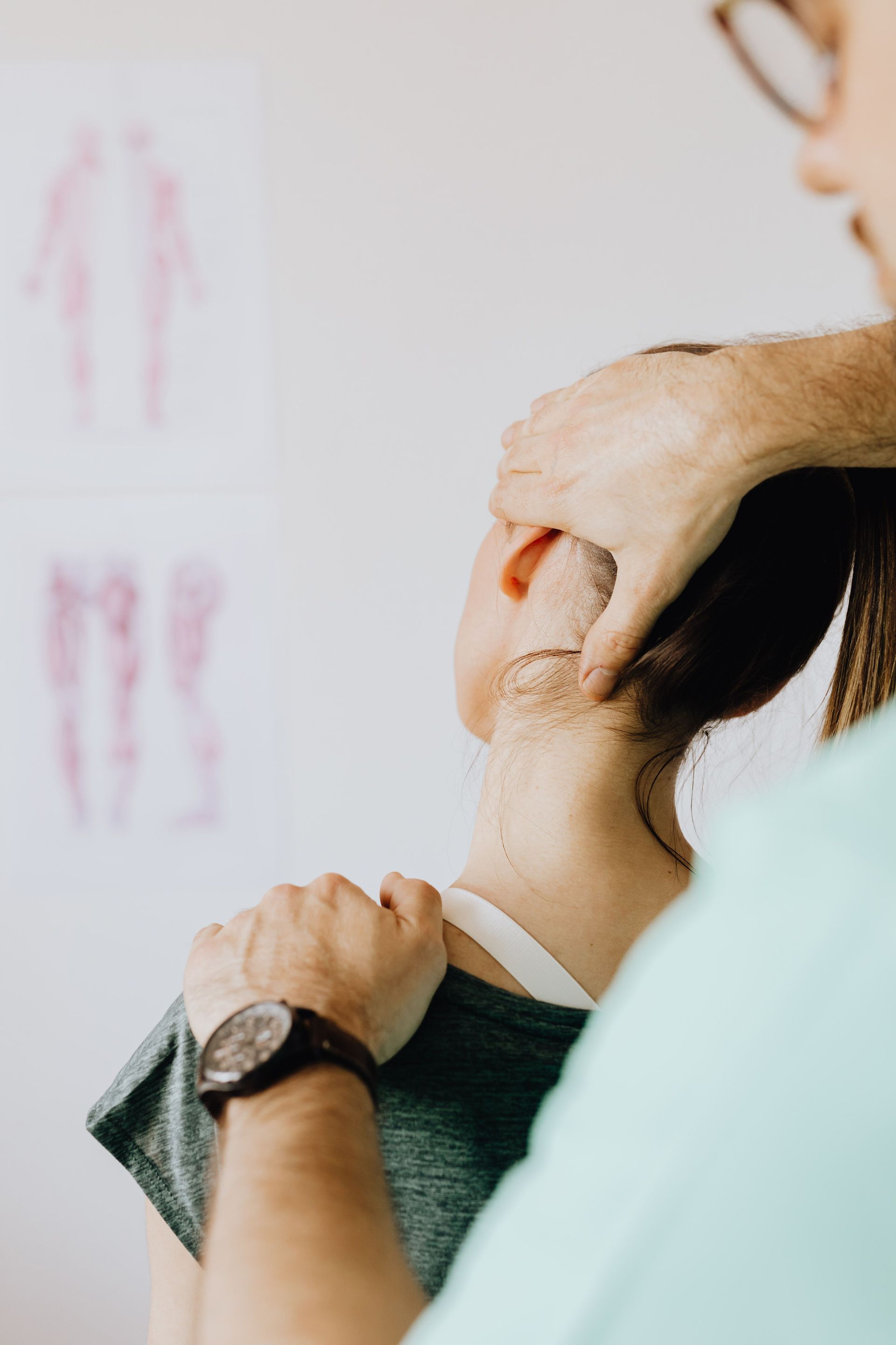 Back view of crop osteopath in uniform and wristwatch checking up neck of slim woman in doctor office in hospital